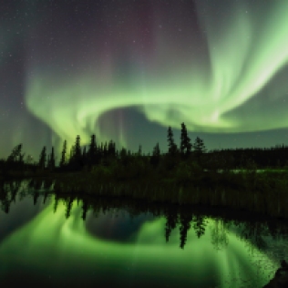 The Aurora Borealis shines brightly on a lake near Yellowknife Canada.